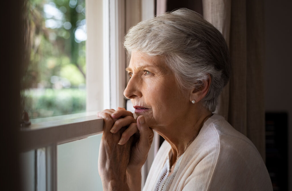 A senior woman looking out the window with a serious expression