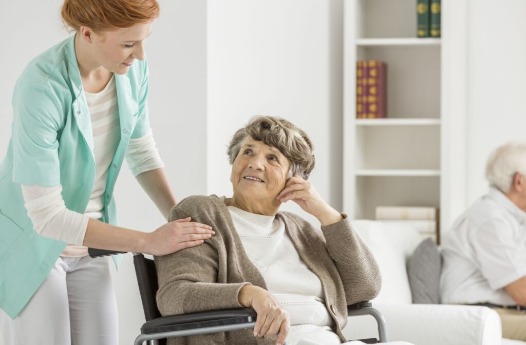 A mature smiling Woman in a wheelchair looks up at a friendly nurse who is offering support.